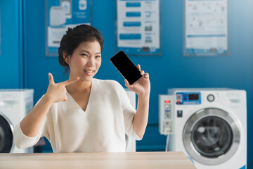 portrait asian female hand use smartphone to check schedule of washing queue in blue color interior laundry shop in condoiminuim city lifestyle