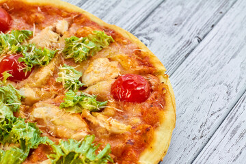 Fresh pizza with chicken, tomatoes and cheese on a light wooden background. Close-up, selective focus