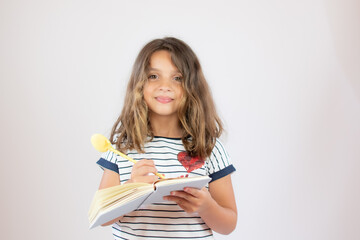 Pretty little girl in striped shirt writing in a notebook