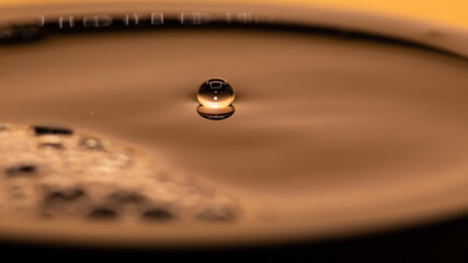 close up drop in a cup of hot black coffee, amber light of dawn