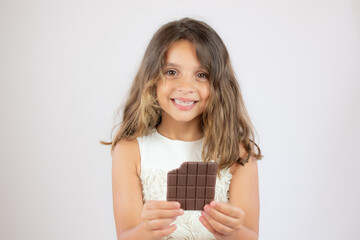 Pretty little girl in white dress eating a chocolate bar