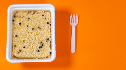 Close up of instant noodles with condiment on orange background. Hot water is poured into plate with macaroni and peppers.