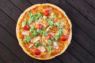 Fresh pizza with chicken, tomatoes and cheese on a dark wooden background. Close-up, selective focus