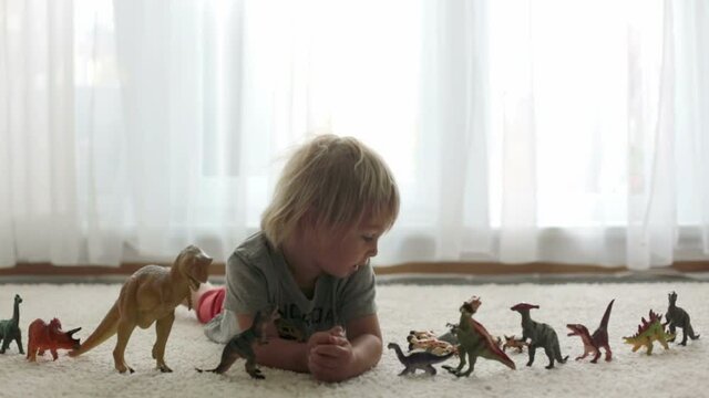 Blond toddler child, playing with dinosaurs at home, nice soft back light