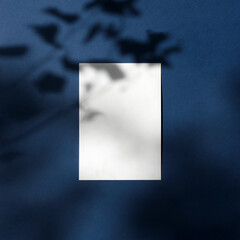Empty white paper a4 mock up with leaves shadows on blue background. Classic Blue Pantone color....