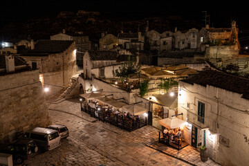Evening view of the city of Matera, Italy, with the colorful lights highlighting patios of sidewalk cafes in the Sassi di Matera a historic district in the city of Matera. Basilicata. Italy