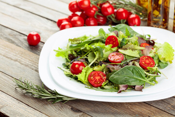 Fresh mixed salad with cherry tomatoes on white plate.