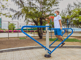 Man doing physical exercises, push ups, strength exercises, leans in empty outdoor public city park metal gym wearing mask alone for Covid19 prevention. Healthy lifestyle in quarantine and coronavirus