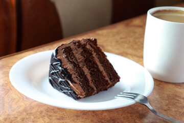 piece of chocolate cake on a white plate close-up. next to a fork and a cup of coffee. horizontal