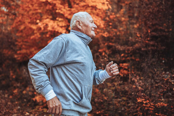 Obraz premium Senior runner in nature. Elderly sporty man running in forest during morning workout. Healthy and active lifestyle at any age concept