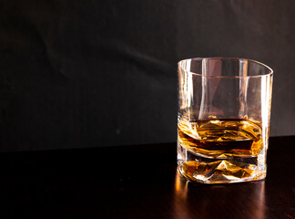 Glasses of whiskey with ice on wooden table and black background. Elegant atmosphere