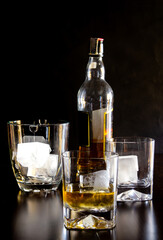 Glasses of whiskey with ice on wooden table and black background. Elegant atmosphere