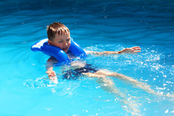 Fototapeta na wymiar A little boy swims in the pool in an inflatable vest. The concept of sport and healthy lifestyle.