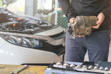 Mechanic man holding starter motor of the car on working table in repair and maintenance garage