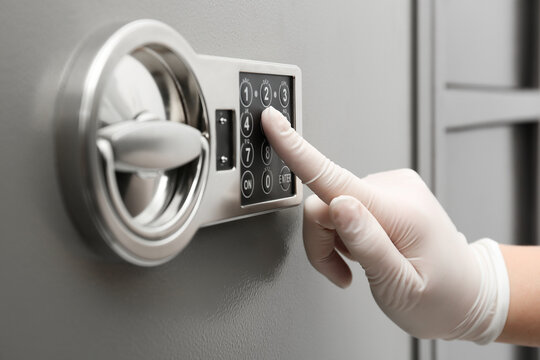 Woman in gloves entering code on keypad of modern safe, closeup