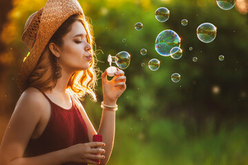 girl in a hat blows soap bubbles in a field at sunset