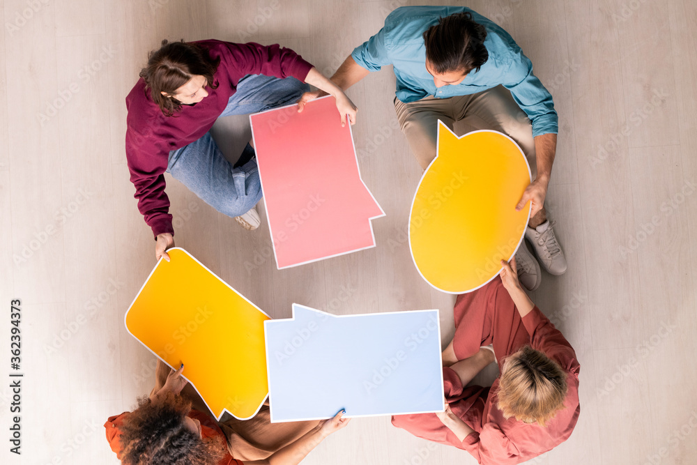 Poster view of four young web designers in casualwear choosing form of speech bubble