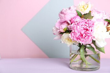 Bouquet of beautiful peonies in vase on lilac table. Space for text