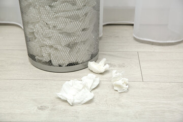 Used paper tissues and trash can on wooden floor