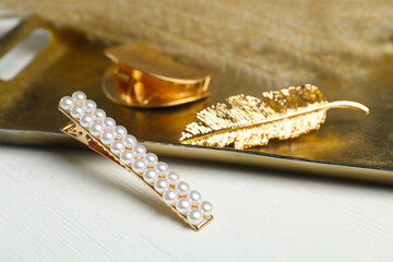 Stylish hair clips and gold tray on white wooden table
