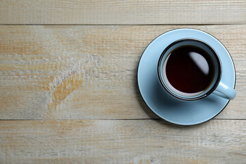 Cup of aromatic black tea on wooden table, top view. Space for text