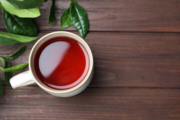 Cup of aromatic black tea and green leaves on wooden table, flat lay. Space for text