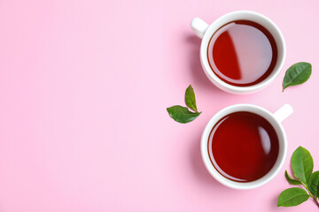 Cups of aromatic black tea and green leaves on pink background, flat lay. Space for text