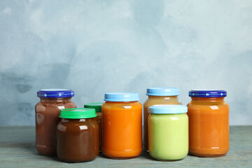 Jars with baby food on wooden table against light blue background