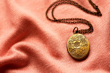 Fototapeta na wymiar old bronze antique locket on a soft pink fabric background, vintage jewelry