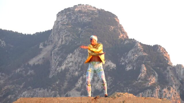 Young bald slender freak man caucasian in tight leggings, gold jacket, bandage on his head, dancing on roof at sunset, runs, has fun, behaves unusually. Slow motion video. Fun, humor, unusual people