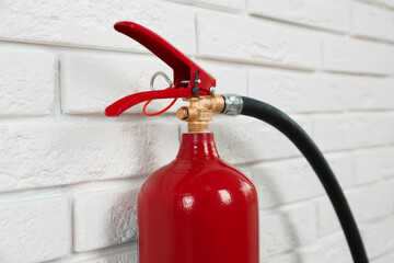 Naklejka premium Fire extinguisher near white brick wall, closeup