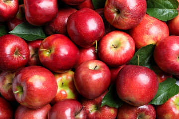 Pile of tasty red apples with leaves as background, top view