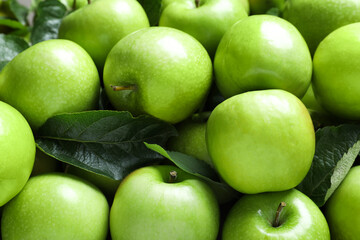 Pile of tasty green apples with leaves as background, closeup