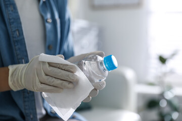 Woman cleaning bottle with wet wipe indoors, closeup. Coronavirus pandemic