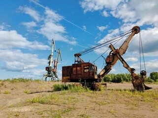 Fototapeta na wymiar old excavator and two large cranes on a background of cloudy blue sky