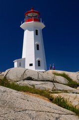 Fototapeta na wymiar Peggys Cove white lighthouse against a blue sky with mother and daughter tourists