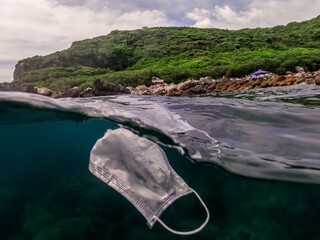 Medical face mask floating underwater. Used surgical mask on ocean water