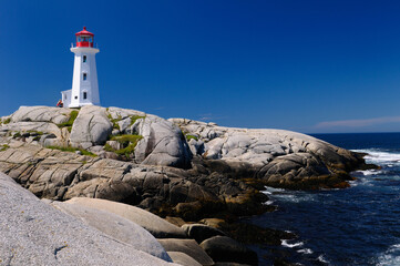 Fototapeta na wymiar Peggys Cove Nova Scotia lighthouse on smooth granite rocks with accordian player and surf