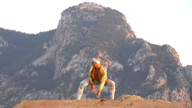 Young bald slender freak man caucasian in tight leggings, gold jacket, bandage on his head, dancing on roof at sunset, runs, has fun, behaves unusually. Slow motion video. Fun, humor, unusual people