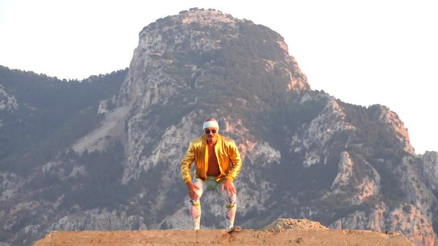 Young bald slender freak man caucasian in tight leggings, gold jacket, bandage on his head, dancing on roof at sunset, runs, has fun, behaves unusually. Slow motion video. Fun, humor, unusual people