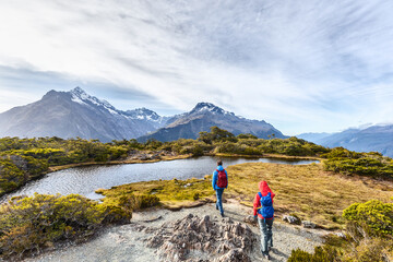 Fototapeta na wymiar Hiking couple walking on adventure hike at Routeburn Track during sunny day. Hikers carrying backpacks tramping on Key Summit Track. People on vacation at Fiordland National Park, New Zealand.