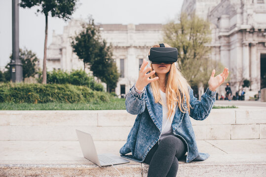Young caucasian blonde woman using vr goggles - Young woman sitting outdoors gesturing watching video with 3d viewer - future, entertainment, virtual reality concept