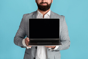 Unrecognizable businessman holding laptop with blank screen on blue background, space for your design