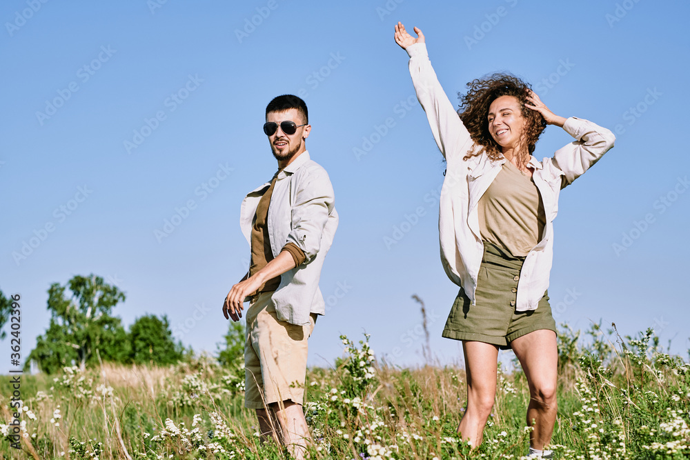 Canvas Prints Pretty young woman dancing in grass against blue sky and expressing gladness