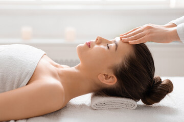 Massage therapist rubbing woman forehead, spa salon interior