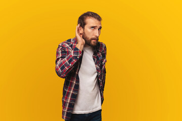 Curious young bearded man in a shirt overhears gossip or tries to hear a secret