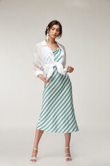 Sexy fashion model beautiful woman pretty face makeup, tanned skin wear summer collection clothes style for romantic date walk trendy light silk in white green stripes long dress white shirt earrings.