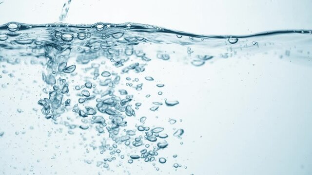 Brilliant stream of water in slow motion falls on smooth clean surface, creating air bubbles, drop splashes and ripples after falling, side view. Freshness of a clear blue liquid on white background