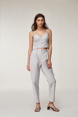 Fashion pretty woman beautiful makeup perfect body shape tanned skin wear clothes summer collection organic textile cotton light gray suit crop top and trousers stylish sandals shoes.