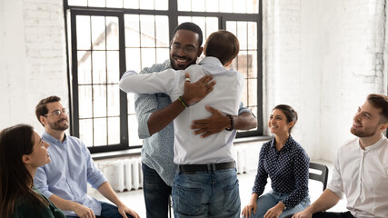 African and Caucasian millennial men embracing during group counselling therapy session. Multi ethnic people gather together provide each other psychological help, overcome problems addiction concept - obrazy, fototapety, plakaty